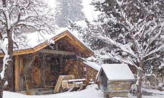 A cozy wooden house in the snow, surrounded by snow-covered trees. The scene depicts a tranquil winter landscape with heavy snowfall.