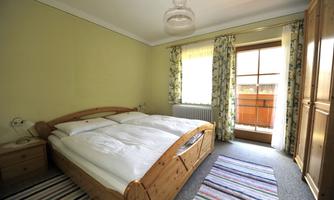 A cozy bedroom with a wooden bed and blooming curtains. The window lets in daylight and offers a view outside.