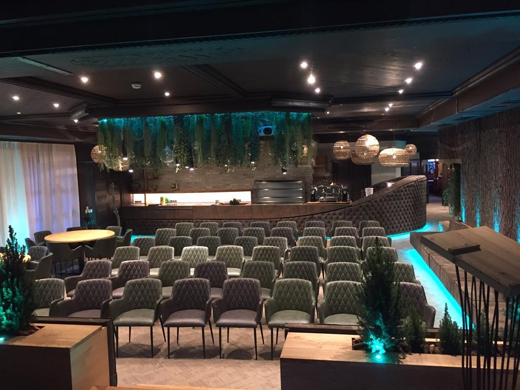 An elegant event space with many green chairs and a modern bar in the background. The soft lighting and plants create an inviting atmosphere.