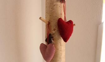 A beautiful tree with three heart pendants. The hearts are red and checked, and they hang from a natural surface.