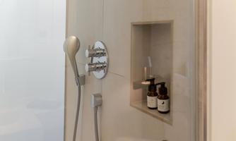 A modern shower cabin with chrome fittings. In the wall shelf, care products are discreetly placed.