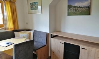 A cozy dining area with a bench and a table. Pictures are hanging on the wall, and there is a wooden cabinet next to the table.