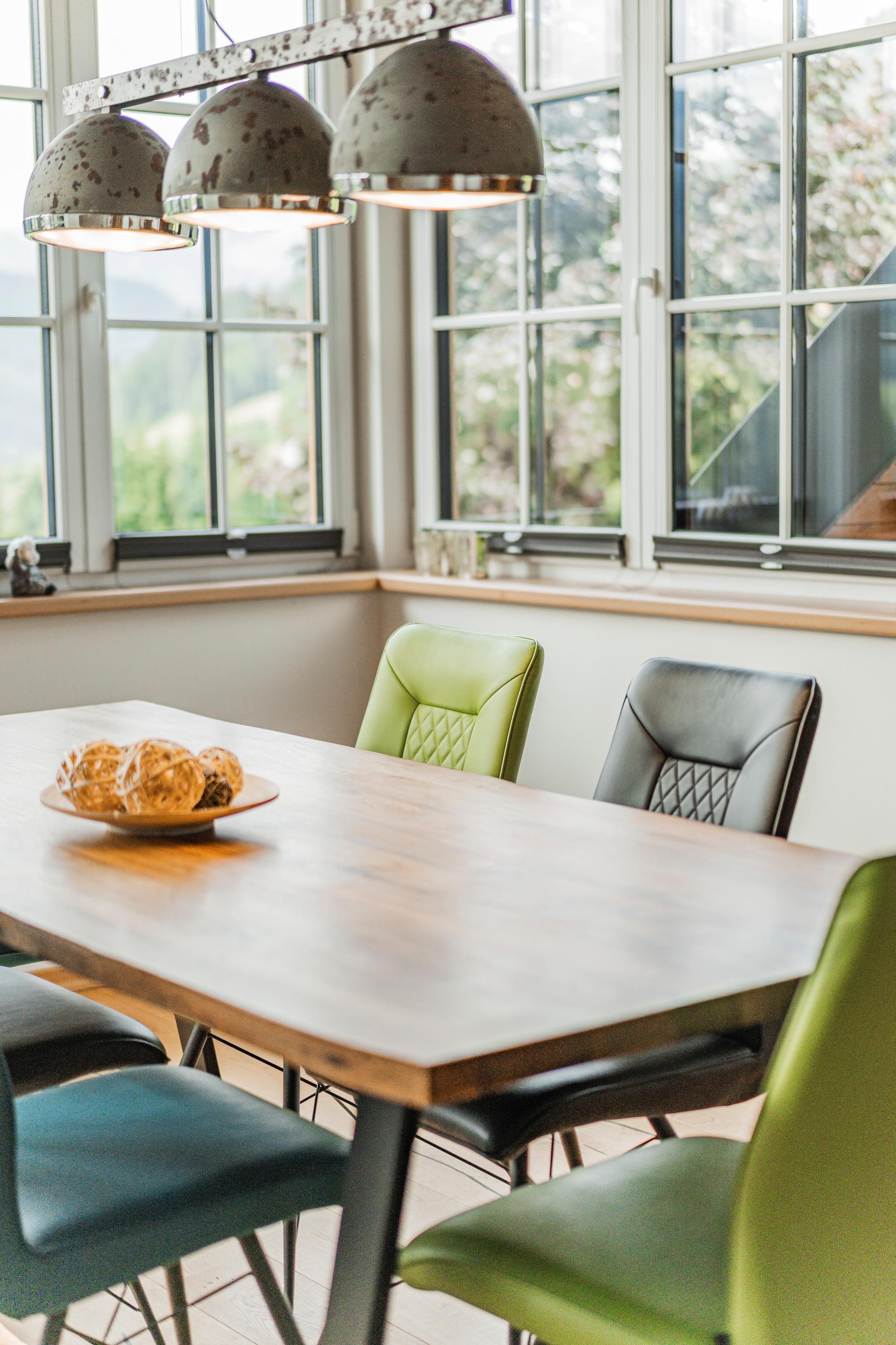 A modern dining area with a wooden log table and colorful chairs. Pendant lights provide warm illumination and create an inviting atmosphere.
