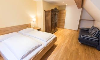 A modern bedroom with a double bed and a wooden wardrobe. The room has a light wood floor and offers a cozy atmosphere.