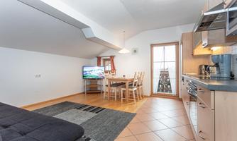 A modern living room with a kitchenette and a dining table. The room is bright and cozy, with a television and access to a balcony.