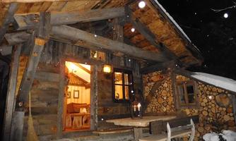 A cozy wooden cabin in the snow at night. Warm light radiates from the windows, giving the scene an inviting atmosphere.