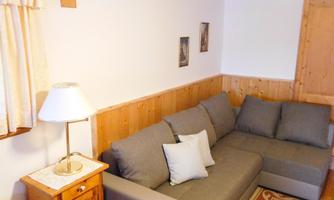A cozy living room with a gray sofa and a floor lamp. The walls are partly made of wood, and some pictures are hanging.