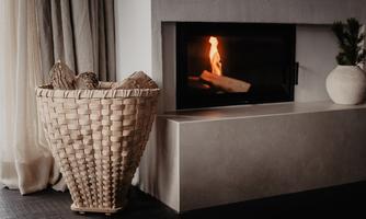 A cozy room with an open fireplace and wood basket. The atmosphere is warm and inviting.