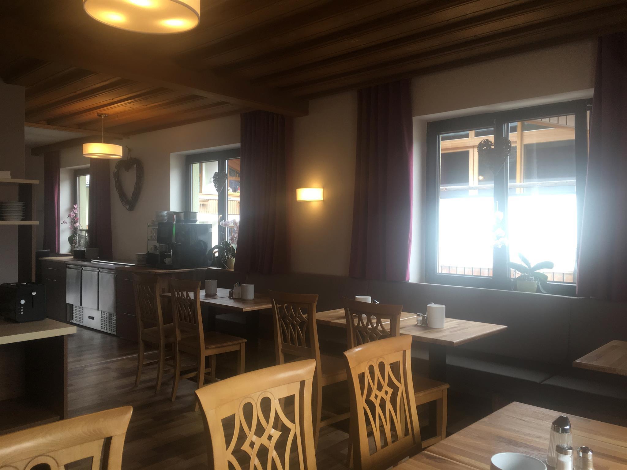 A cozy interior with wooden chairs and tables. The windows let in plenty of light and provide a pleasant atmosphere.