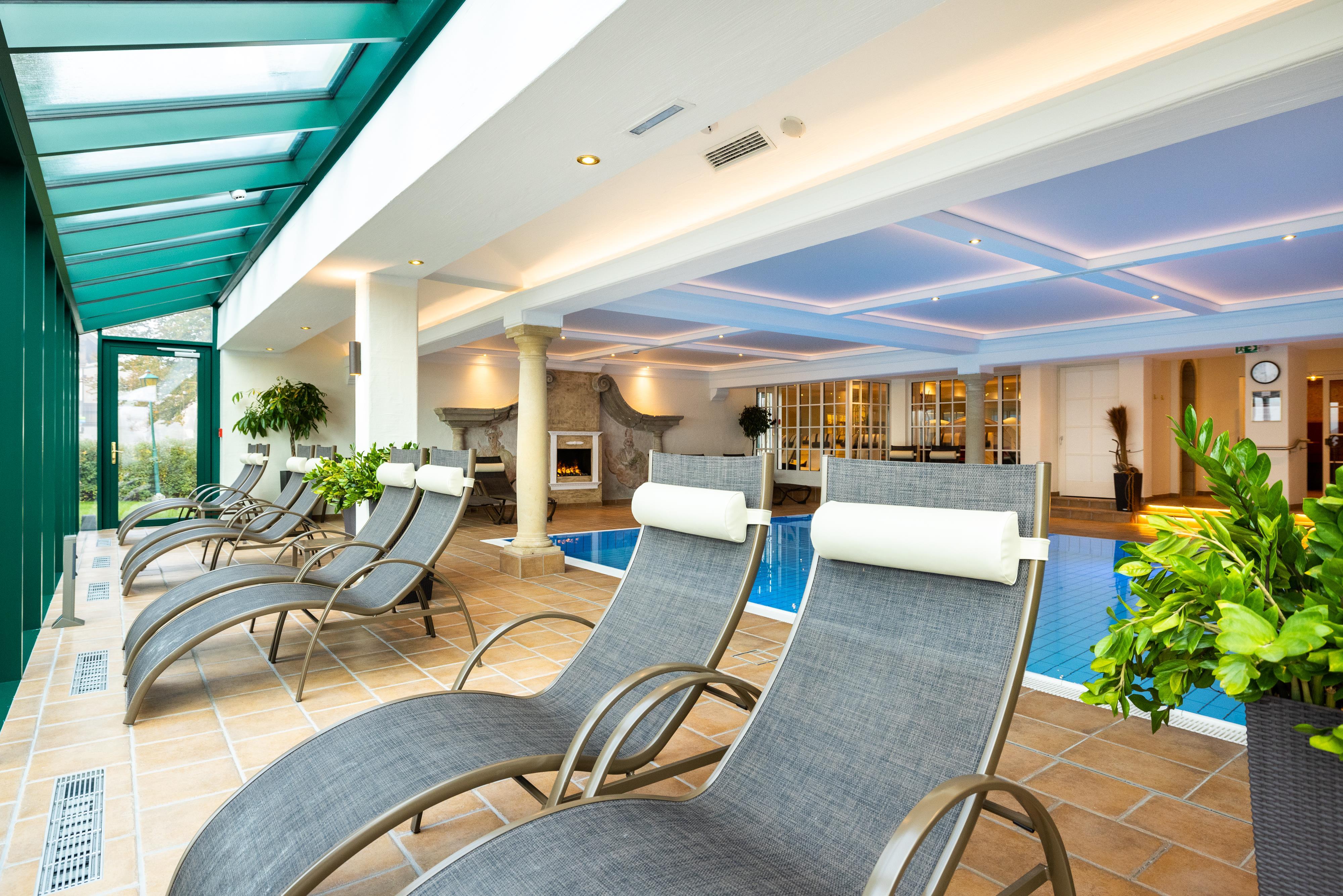 An elegant wellness area with loungers and a pool. The bright colors and plants create a relaxed atmosphere.