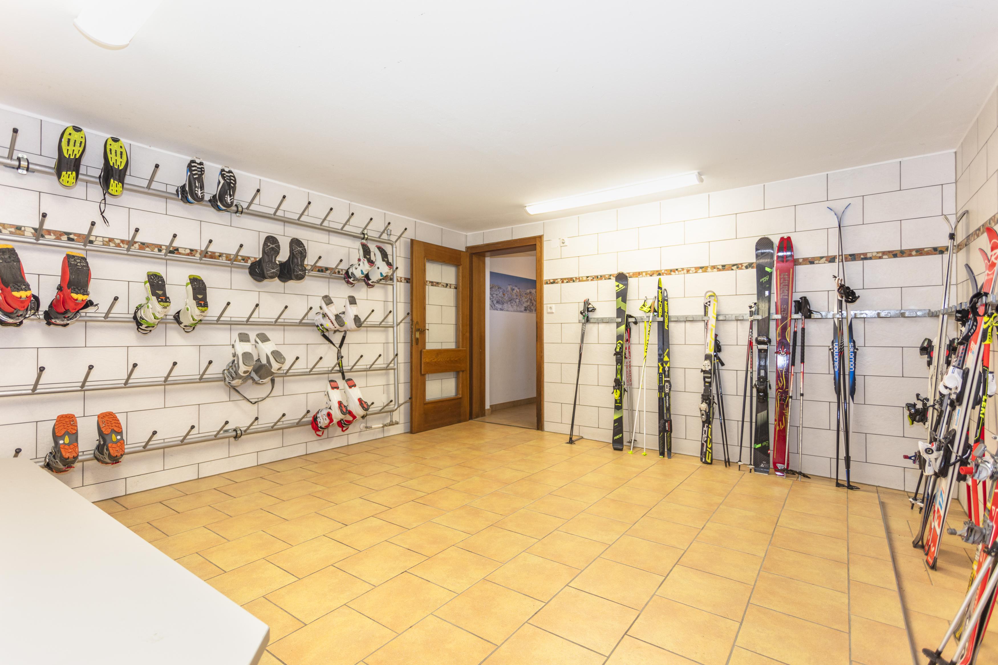 A room with walls equipped with skis and ski equipment. A bright, open space with tiled flooring and a door in the background.