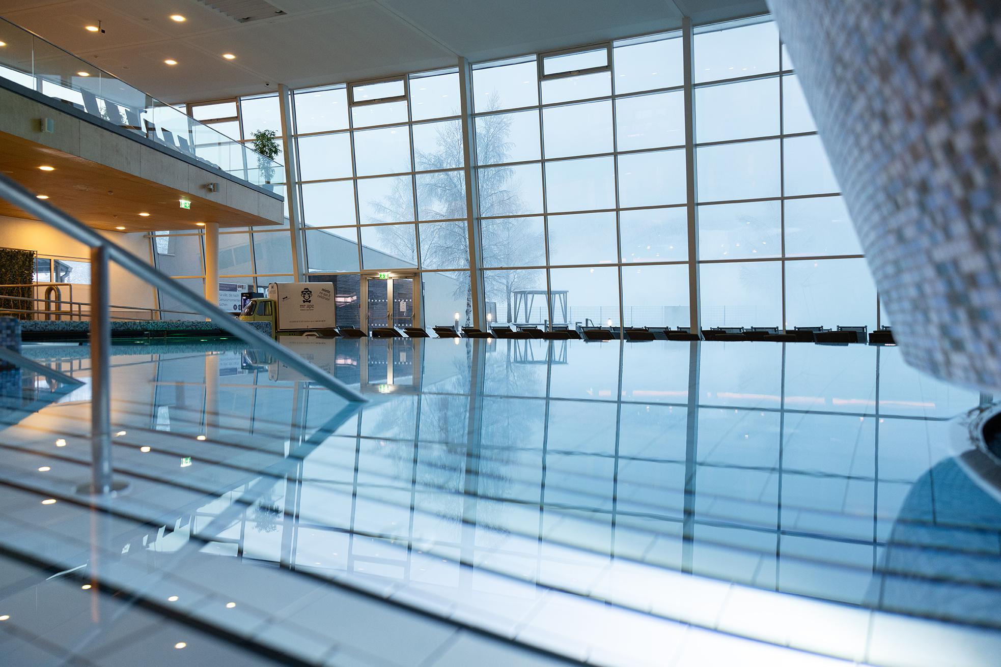A modern swimming pool with large windows and natural light. The water reflects the surroundings and creates a relaxing atmosphere.