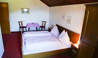 A cozy room with two beds and a table. The walls are bright, and there are wooden details as well as fresh decorations.
