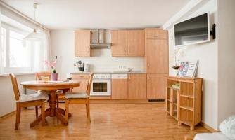 A modern kitchen with a dining table and chairs. The room is bright and friendly with wooden flooring and a large window front.