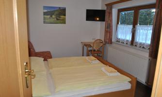 A cozy room with a double bed and bright bedding. There is a television, a table and chairs, as well as a window with a view.