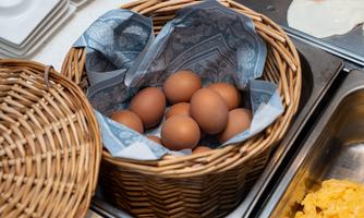 A basket with brown eggs, beautifully wrapped in decorative paper. In the background, some additional breakfast ingredients are visible.