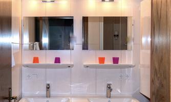 A modern bathroom with two sinks and large mirrors. Colorful cups are on the shelves above the sinks.