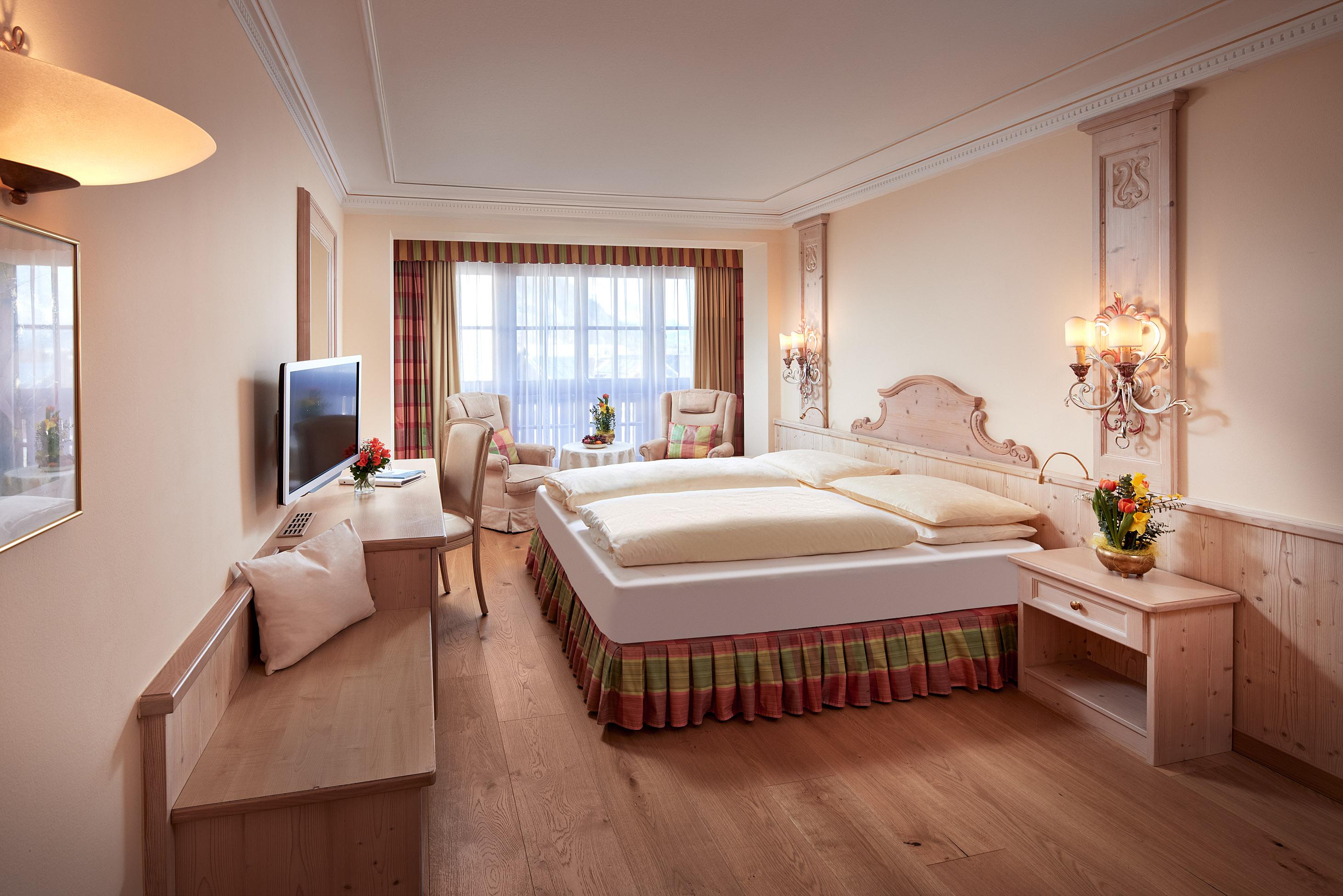 A modern bedroom with a cozy bed and wooden floor. Large windows let in plenty of light, and the decoration is elegant and inviting.