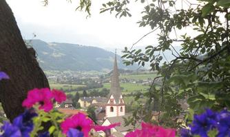 A picturesque landscape with a church and a pointed tower in the background. Colorful flower frames emphasize the scene.