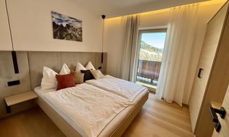 A modern bedroom with a double bed and bright walls. Large windows offer a view of the mountains and let in plenty of daylight.