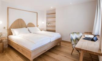 A modern bedroom with a cozy wooden bed and two mattresses. There is a desk and shelves on the wall.