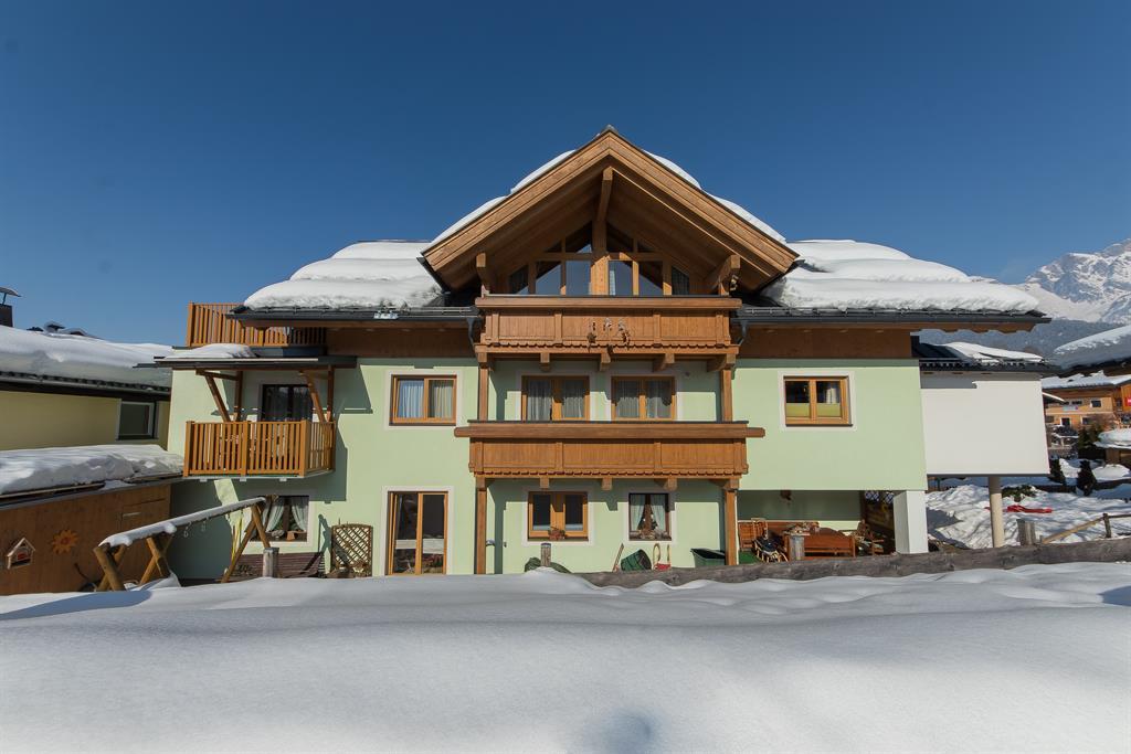 A charming house with wooden siding and several balconies, surrounded by snow. The clear blue sky creates a friendly atmosphere.
