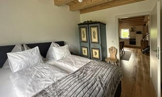 A cozy bedroom with two beds, a gray duvet, and a wooden floor. In the background, a kitchen area is visible.