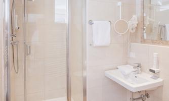 A modern bathroom with a glass shower and a small sink. The walls are light-tiled and there are soft towels.