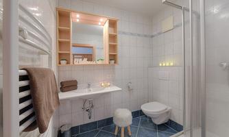 A modern bathroom with white tiles and a clear shower. The space is well-lit and has a cozy atmosphere.