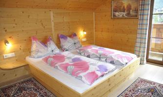 A cozy bedroom with two single beds and colorful pillows. The walls are made of wood, and a carpet lies on the floor.