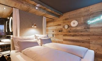 A modern bedroom with a comfortable bed and rustic wooden walls. Soft lighting and decorative elements create a cozy atmosphere.