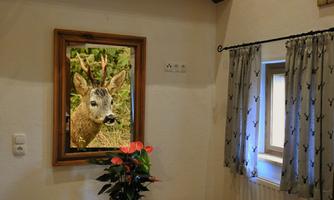 A beautiful room with a picture of a deer in a frame on the wall. A flower pot with plants is on the table.
