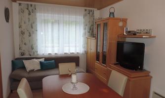 A cozy living space with a dining area and a sofa. Large windows provide plenty of daylight.