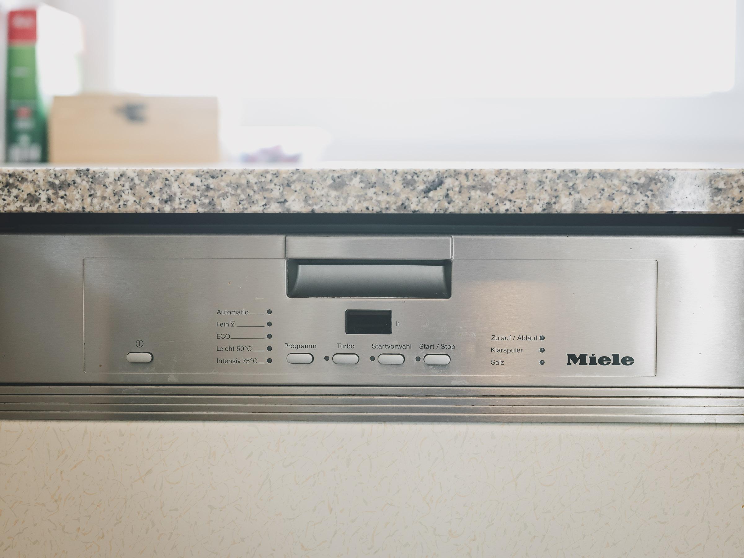 A modern dishwasher from Miele with a silver control panel. The surface is made of gray granite.