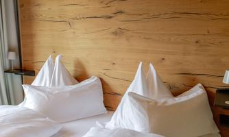 A cozy bedroom with two beds and white pillows. The wooden wall gives the room a warm atmosphere.