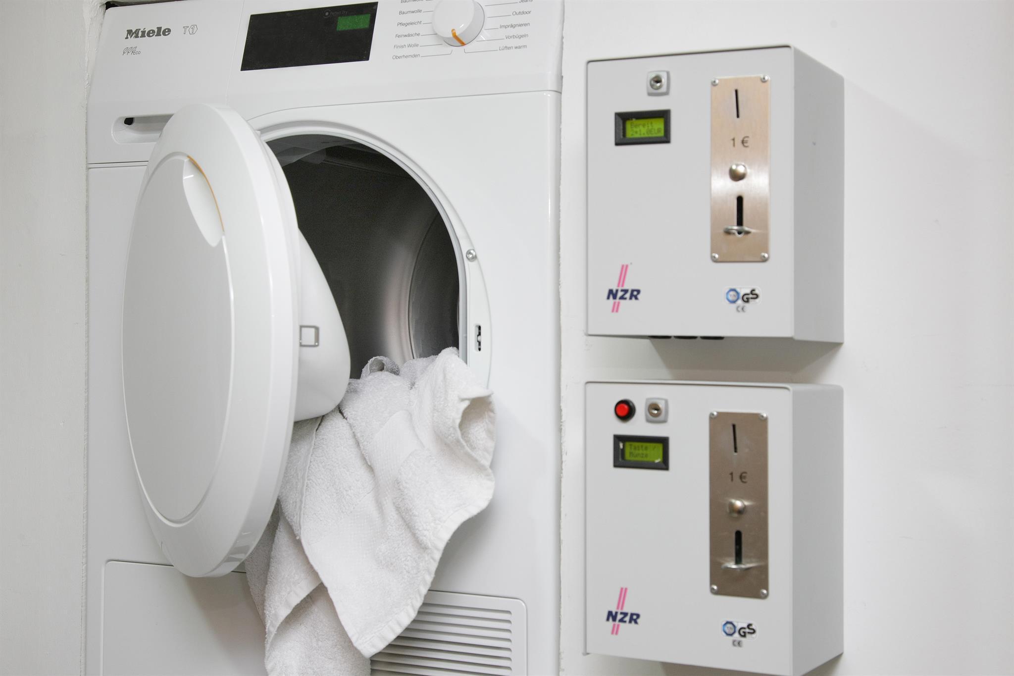 A dryer with an open door and a white towel. Two control units are mounted on the wall.
