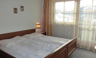 A bright bedroom with a double bed and a cozy atmosphere. The windows are fitted with curtains and blinds and let in plenty of daylight.