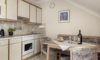 A bright kitchen with modern furniture and a dining table. On the table, there are some fruits and a bottle of wine.