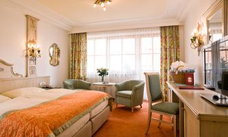 A cozy hotel room with a double bed and two armchairs. The large windows let in plenty of light and create an inviting atmosphere.