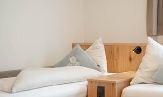 A cozy room with two beds made of light wood. The pillows are inviting and the walls are bright and plain.
