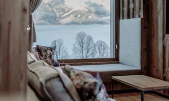 A cozy living room with a large window view of the mountains and the lake. The wooden details create a warm atmosphere.