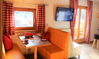 A cozy living room with an orange seating area and a wooden table. Large windows let in plenty of light and showcase a winter landscape outside.