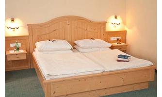 A cozy bedroom with a large wooden bed and two nightstands. On the bed, there are pillows and a blanket, while a book and a water bottle are on the blanket.