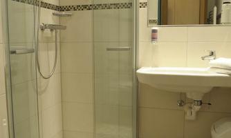A modern bathroom with a shower and toilet. The walls are light tiled and there is a sink with a large mirror.