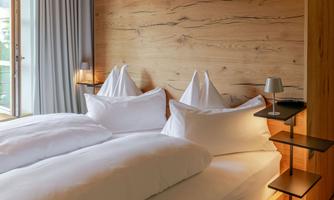 A modern bedroom with two double beds and wood paneling. Large windows let in plenty of daylight.