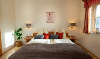 A cozy bedroom with a large bed and colorful pillows. Soft lighting and a plant create a pleasant atmosphere.