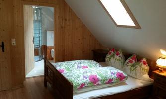 A cozy bedroom with a double bed and colorful cushions. In the background, a modern bathroom is visible.