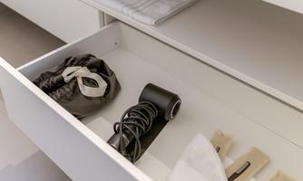 An open drawer with various items. Among them are a black-and-white roll, a fabric bag, and some wooden clips.
