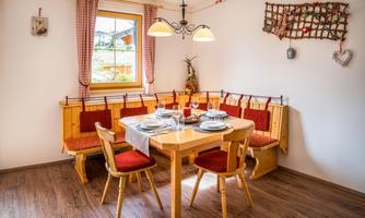A cozy dining area with a wooden table and red seat cushions. The walls are light, and a window lets in plenty of light.