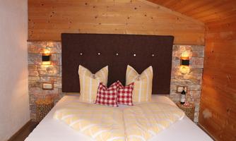 A cozy bedroom with a large bed and decorative pillows. The walls are made of wood and stone, creating a warm atmosphere.